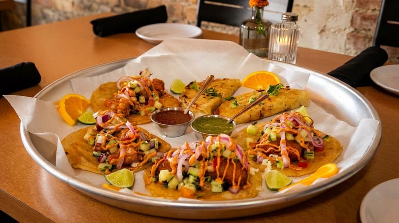 A large platter of tacos and quesadillas with various toppings, salsas, and citrus wedges.