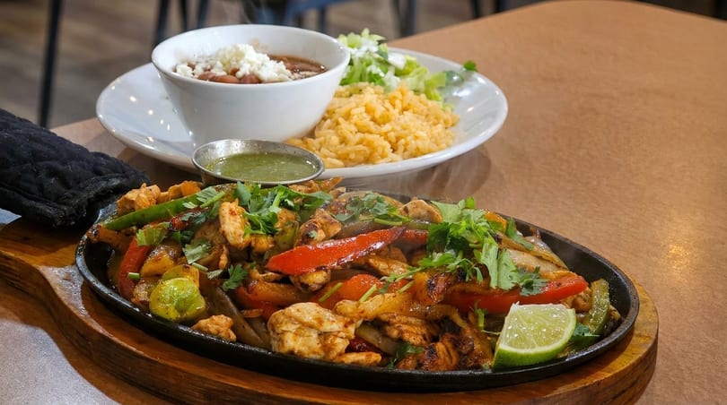 Sizzling chicken fajitas with peppers and onions, served with rice, beans, and salsa.